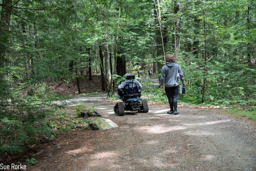 Man in trail wheelchair goes down trail with friend
