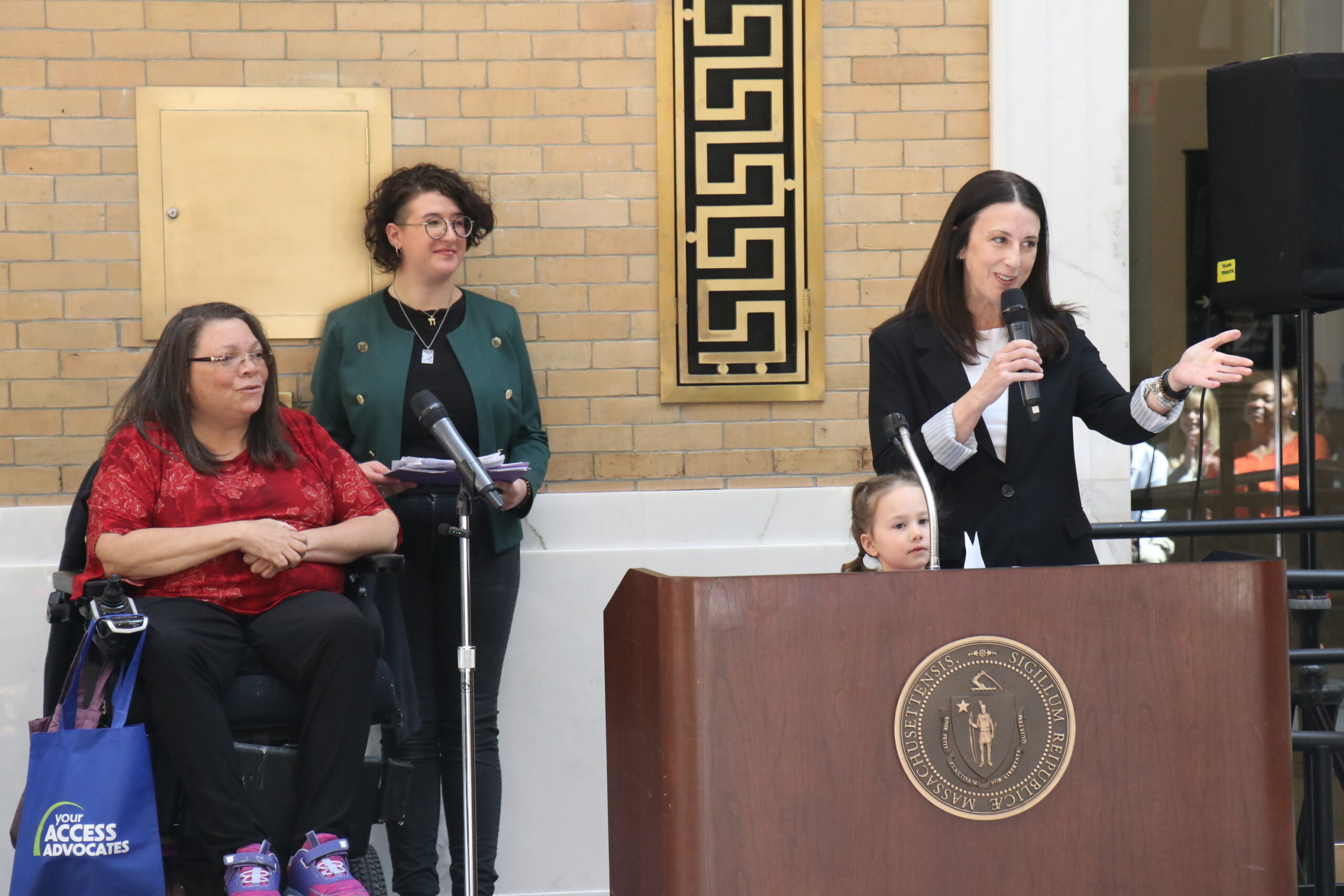 Senator Robyn Kennedy speaking at a podium and smiling, Rachael Cowan and Nancy Garr-Colzie smiling behind her