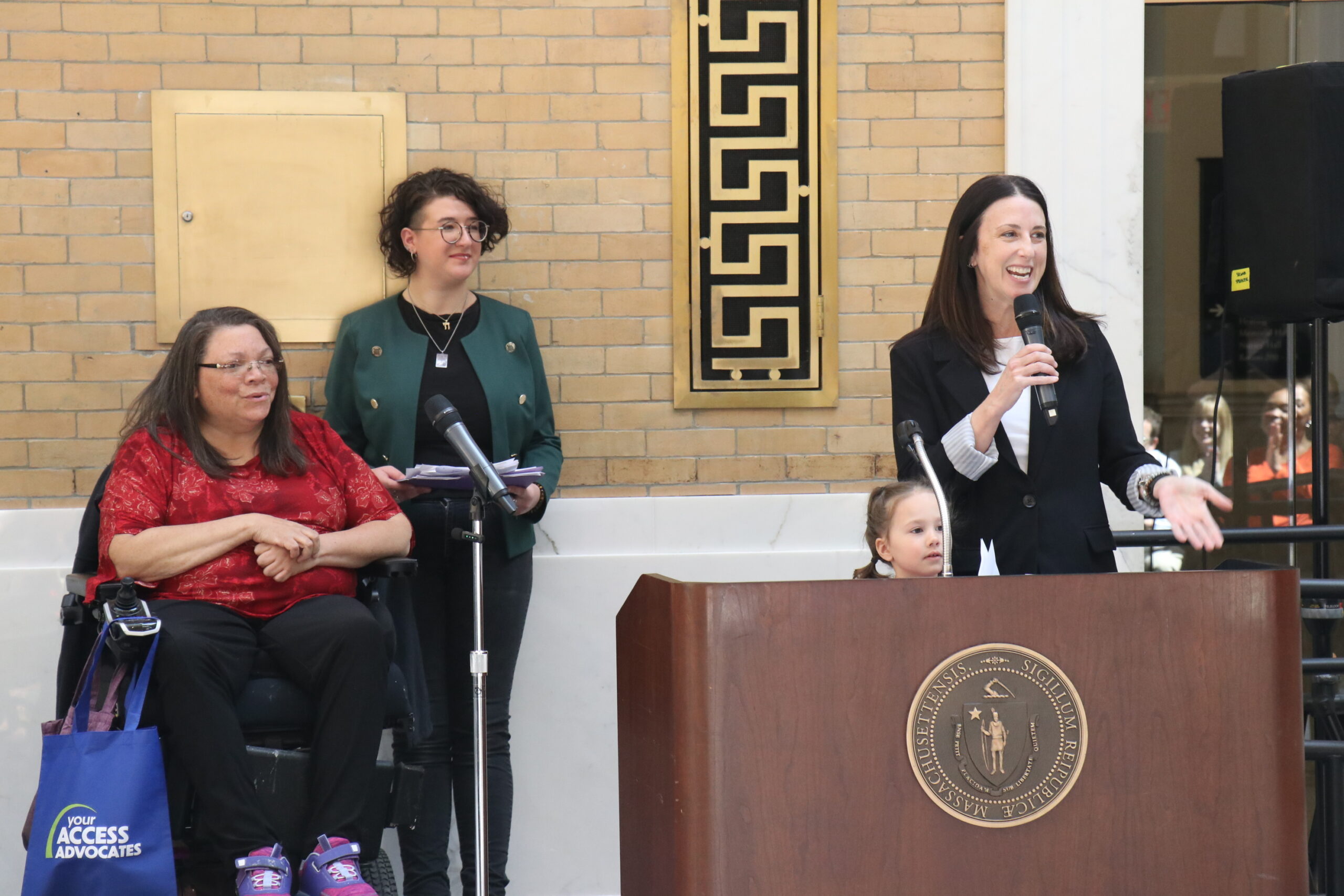 Senator Robyn Kennedy speaking at a podium and smiling, Rachael Cowan and Nancy Garr-Colzie smiling behind her