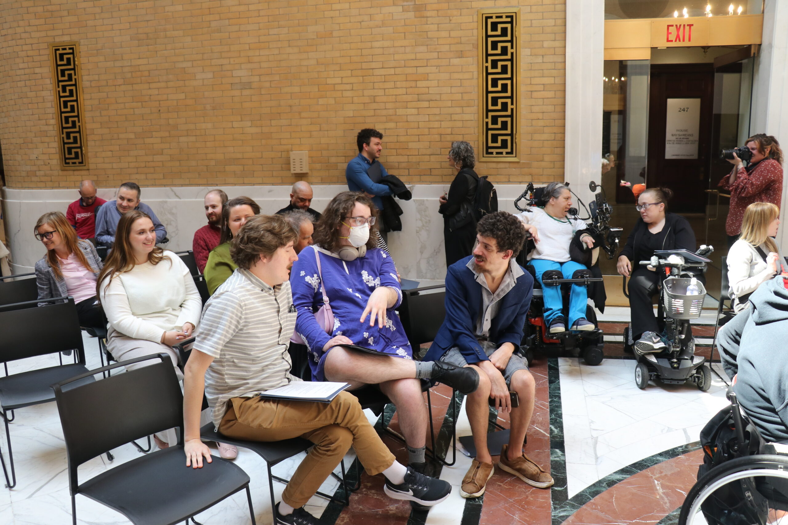 three people talking and gesturing, with others in the background