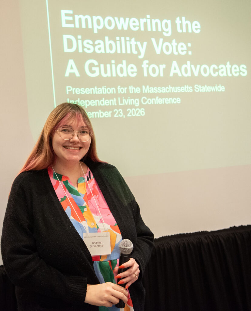 Brianna Zimmerman, Disability Law Center , smiling in front of presentation screen that reads "Empowering the Disability Vote: A Guide for Advocates"